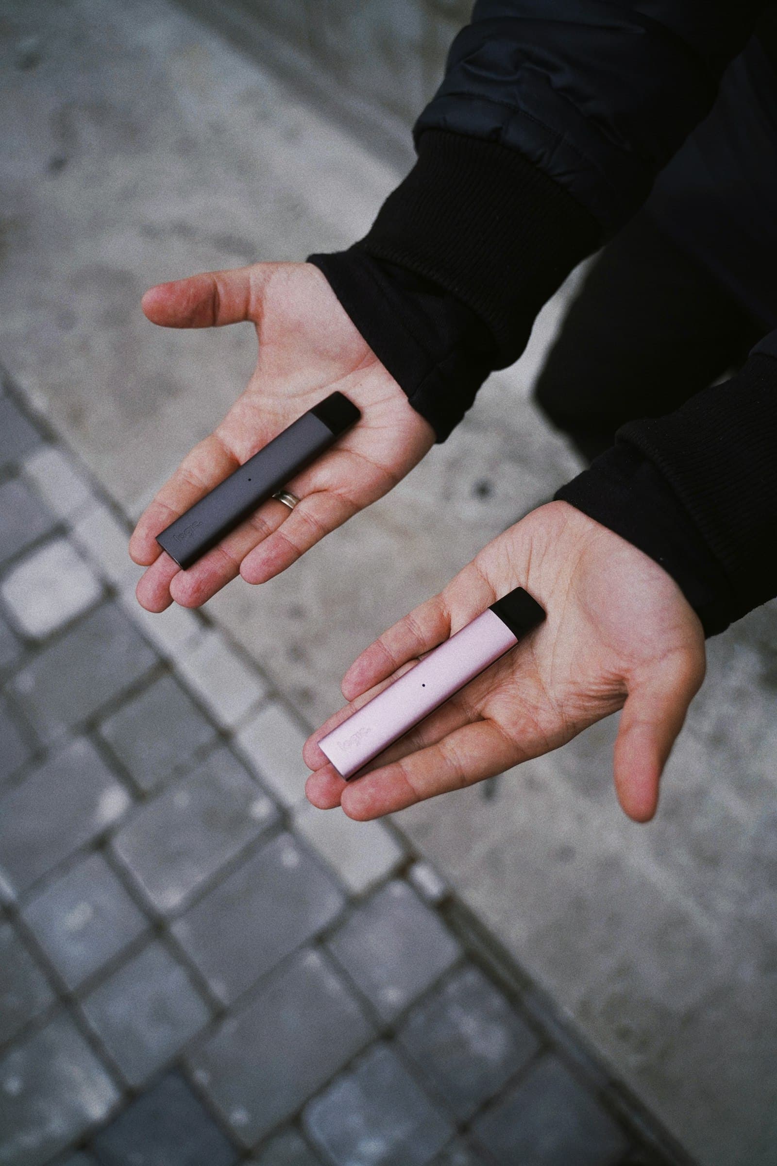 A vaper holding two different pod devices side by side, one in each palm, to compare their size and weight